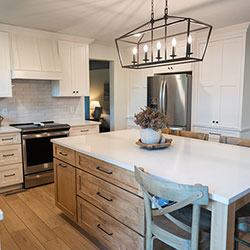 A kitchen interior features white cabinets on the walls and a center island with natural wood-toned drawers