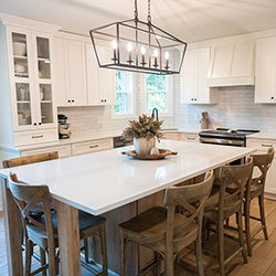 A kitchen interior with white cabinets on the walls, a center island with natural wood-toned drawers, and a glass-paned cabinet that displays dishware and decor