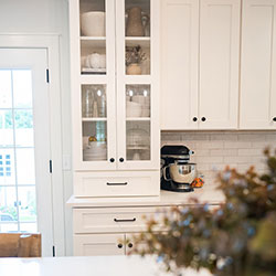 A glass-paned kitchen cabinet holds dishware and decor