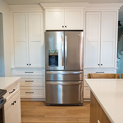 A kitchen interior with white drawers and cabinets that stretch from floor to ceiling and surround a refrigerator