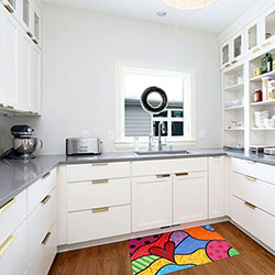 White cabinetry lines the walls of a kitchen, including one wall with open shelves holding dishware and food storage