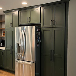 Dark green floor-to-ceiling cabinets surround a refrigerator on the interior of a kitchen