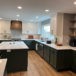 A kitchen interior blends white and dark green cabinets with wood accents