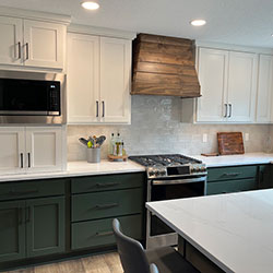 A kitchen interior blends white and dark green cabinets with wood accents