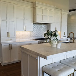 A kitchen interior features all-white cabinetry and a center island with cushioned bar seating