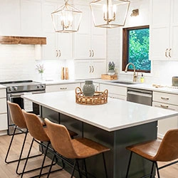 The interior of a kitchen with new white cabinetry along the walls and a center island with bar-style seating